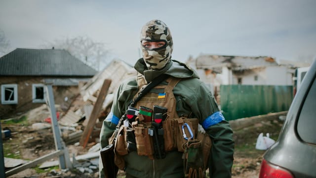 Soldier in camouflage gear standing in Kyiv Oblast, Ukraine amidst destruction.