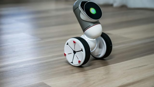 A close-up of a modern, wheeled robot with a digital interface, on a wooden floor.