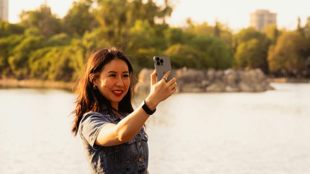A woman taking a selfie by a serene lake, surrounded by trees on a warm summer day in Mexico City.