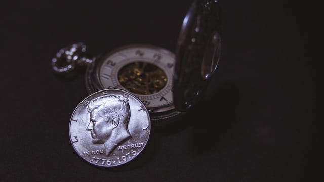 Close-up of a vintage silver coin with a pocket watch, symbolizing time and wealth.