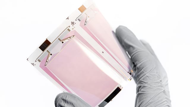 Close-up of a gloved hand holding a flexible display sheet, showcasing cutting-edge technology.