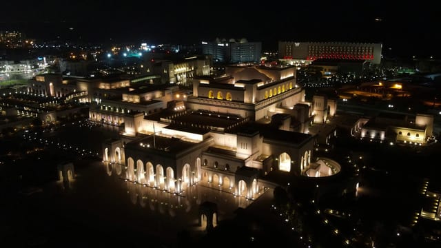 Aerial view of the illuminated Royal Opera House in Muscat at night.