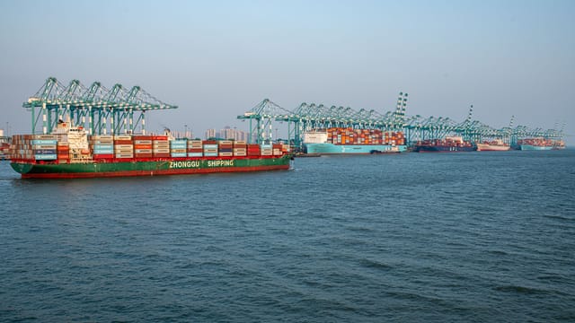 A bustling shipping port featuring container ships and crane operations under clear skies.