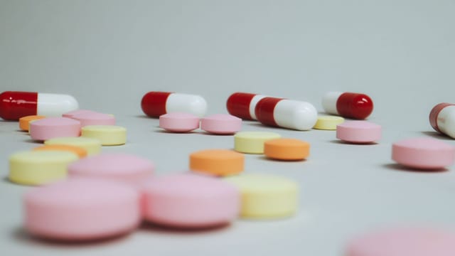Close-up of varied pills and capsules scattered on a white surface.
