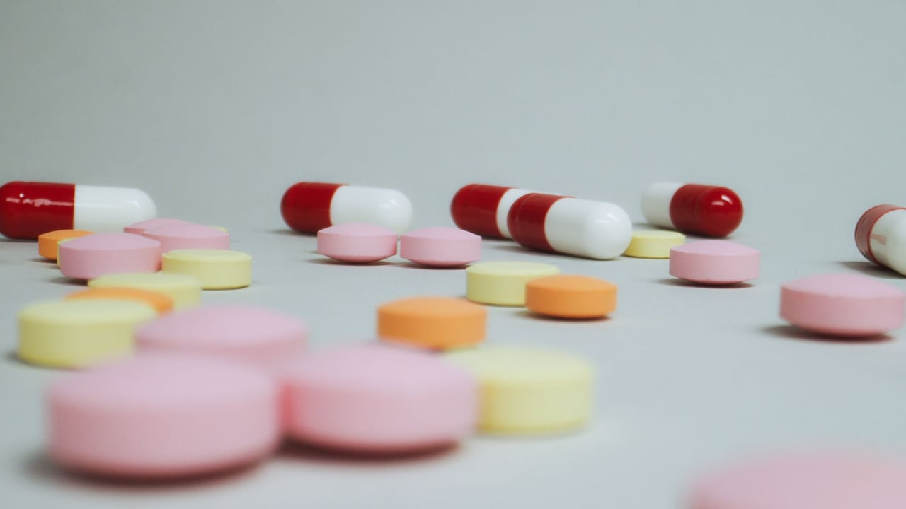 Close-up of varied pills and capsules scattered on a white surface.