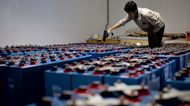 Illustrative image: A worker checking many industrial batteries inside a facility. Indoor, industrial setting.