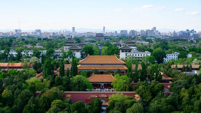 A stunning aerial view of ancient Chinese architecture with Beijing's city skyline in the background.