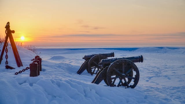 Sunset over snow-covered field with cannons in Архангельская область, Russia.