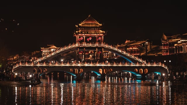 Stunning view of the illuminated Fenghuang Bridge in Xiang Xi, China at night, reflecting on the serene river.