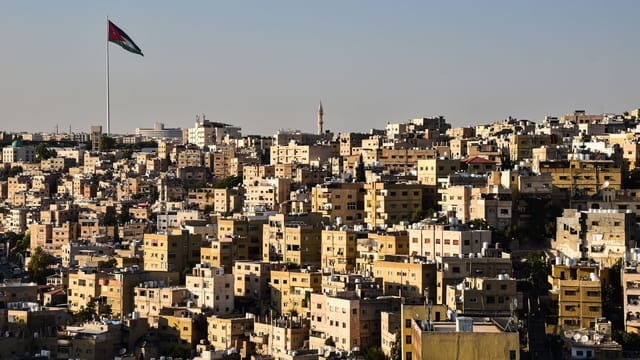 A stunning aerial view of Amman's urban cityscape with the Jordan flag fluttering prominently.