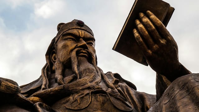 Bronze statue of Guan Yu representing strength and wisdom against cloudy sky.