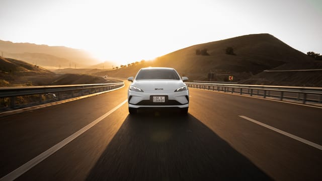 Electric car driving on a scenic highway at sunset, highlighting modern automotive design and sustainable travel.