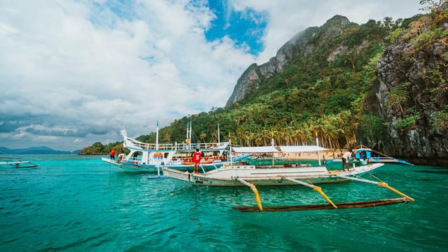 Traditional boats in turquoise waters against lush cliffs in El Nido, Philippines.