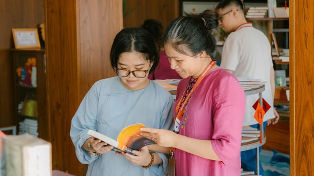 Two women engaged in reading and discussing books inside a modern library setting.