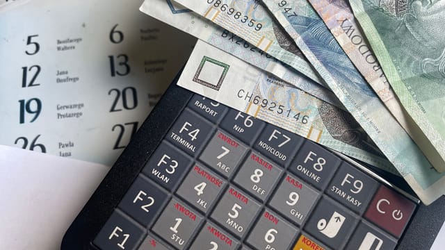 Close-up of Polish Zloty banknotes on a calculator with a calendar in the background.