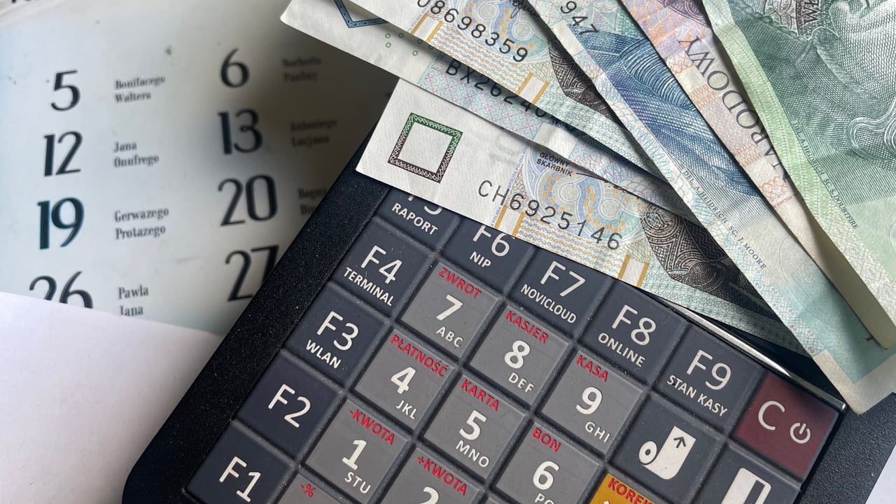 Close-up of Polish Zloty banknotes on a calculator with a calendar in the background.