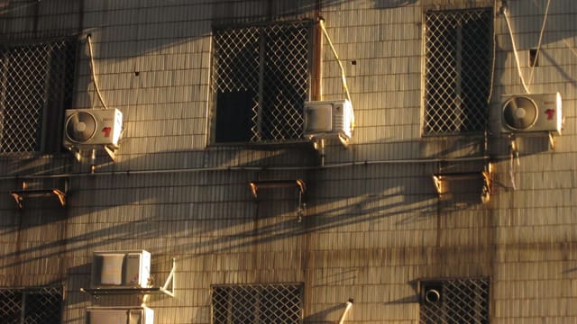 Exterior of urban building with air conditioning units and shadow play on the facade.