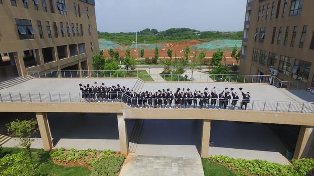 Aerial view of students in graduation gowns on a bridge between buildings.