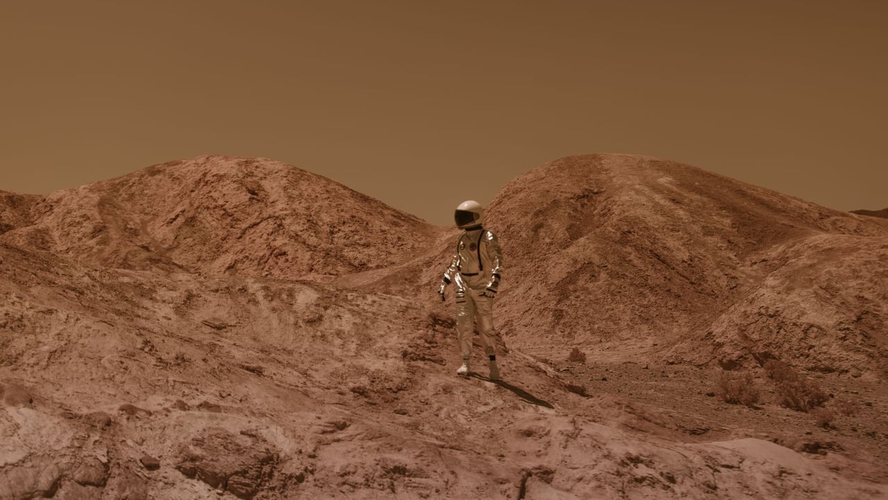 Astronaut in spacesuit explores barren, Mars-like desert terrain under brown sky.