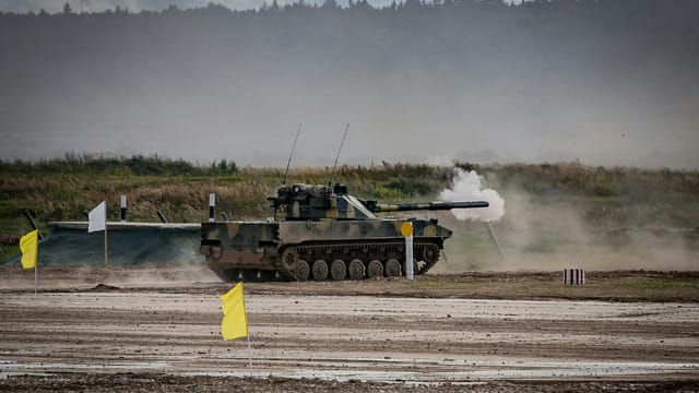 A military tank firing a shell during training in an open field.