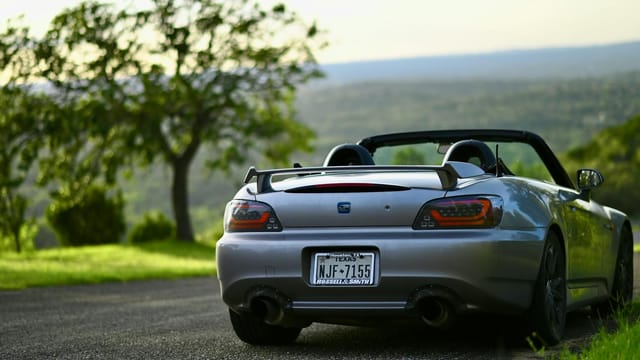 A gray Honda S2000 parked roadside at Canyon Lake, Texas, surrounded by greenery and a serene landscape.