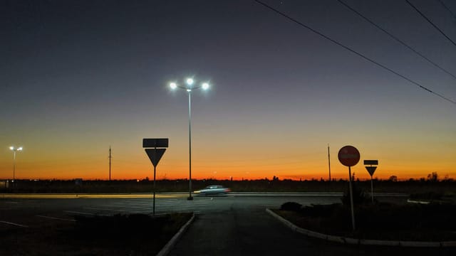 A tranquil road scene during twilight with street lights glowing against a colorful sky.
