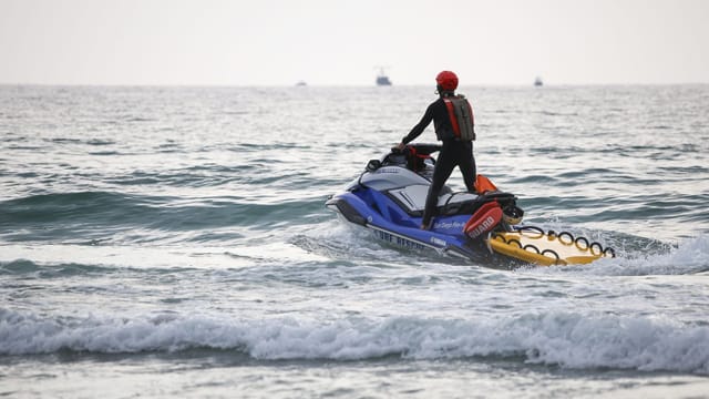 A lifeguard on a jet ski patrols the ocean to ensure swimmer safety during daytime.