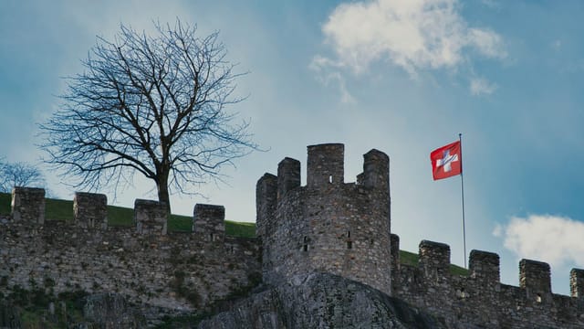 Ancient stone fortress in Switzerland with a Swiss flag and tree in view.
