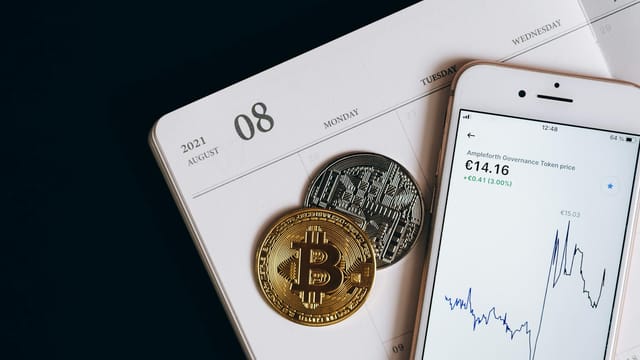 A smartphone displays cryptocurrency data alongside Bitcoin and Ethereum coins on an August calendar.