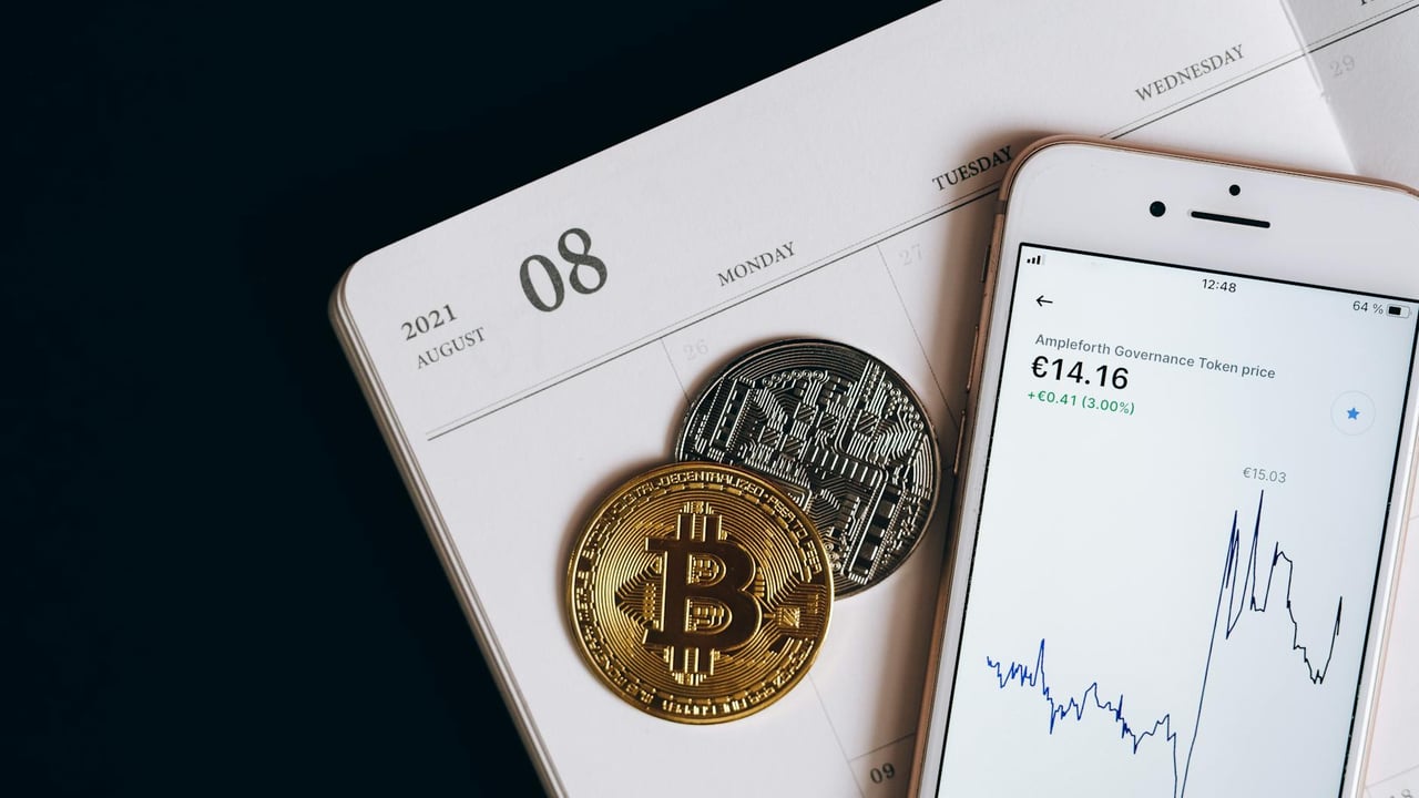 A smartphone displays cryptocurrency data alongside Bitcoin and Ethereum coins on an August calendar.