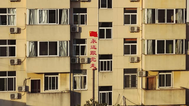 Facade of high building with red Chinese inscription in residential area in light of sun
