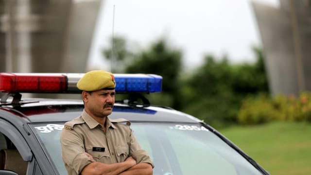 Indian police officer with arms crossed standing by a patrol car outdoors, showcasing authority and law enforcement presence.