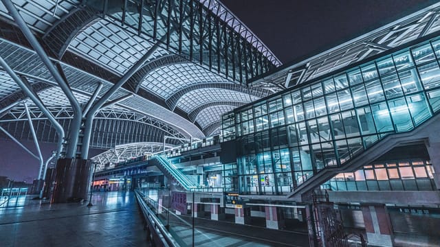 A modern, empty railway station with futuristic architecture featuring glass and steel structures at night.