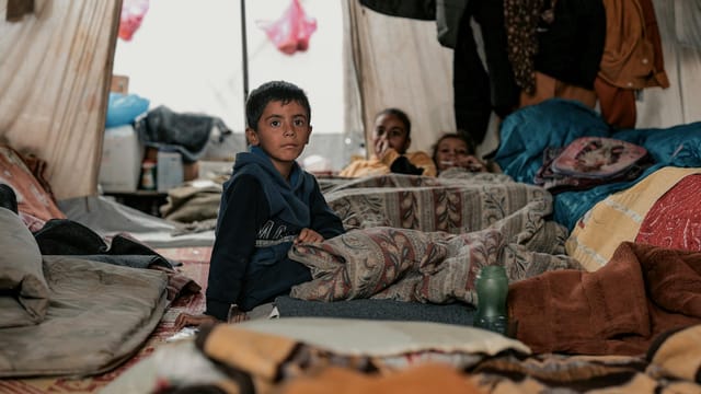 Children sheltered in a tent in Gaza amidst conflict, highlighting resilience and hope.