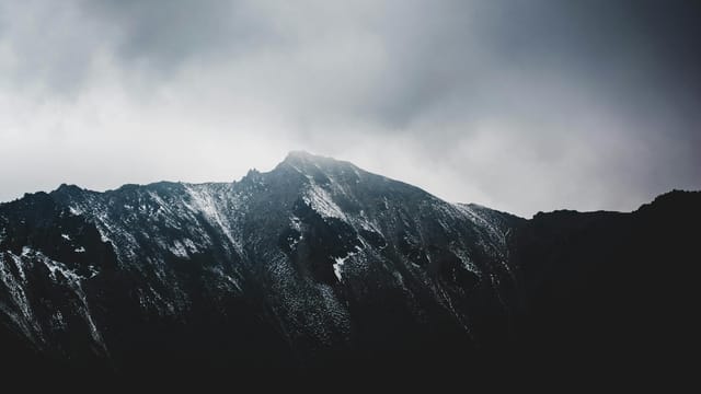 A stunning view of a snow-capped mountain peak with dramatic cloudy skies.