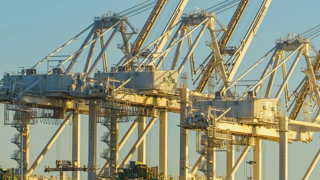 Close-up view of port cranes during sunset at a busy industrial harbor.