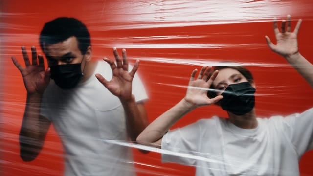 Artistic portrait of two adults in face masks behind plastic, symbolizing pandemic isolation.