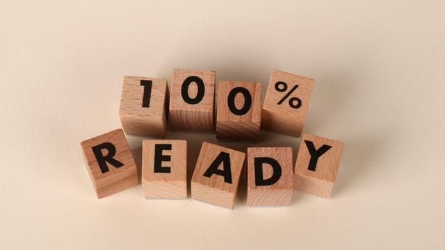 Wooden blocks arranged to show the text '100% Ready' on a neutral background, symbolizing preparedness and confidence.