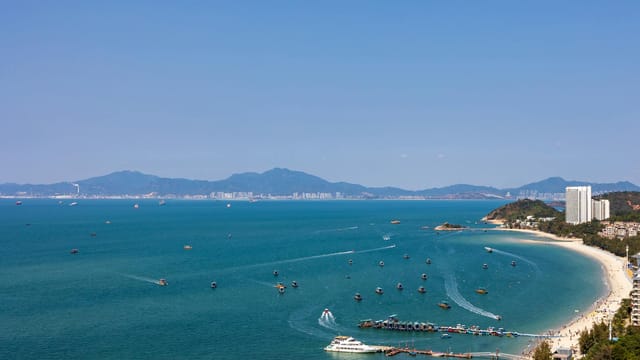 Beautiful beach and coastline in Huizhou, Guangdong, with boats and hills in the distance.