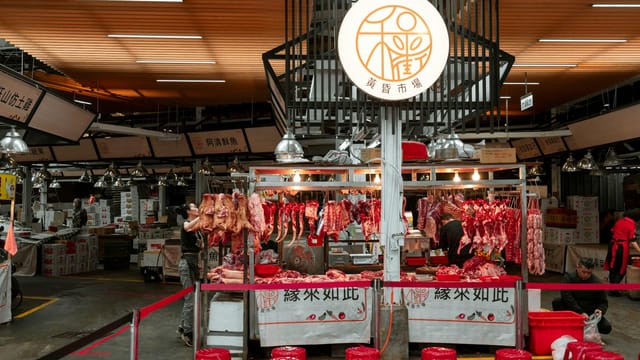 Active Asian market scene showcasing an indoor butcher stall with various meat cuts and vibrant red seating.