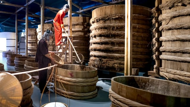Factory employees with wooden buckets near barrels with ropes in fish sauce factory