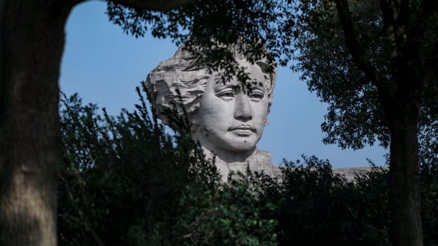 A statue of Mao Zedong emerges through lush greenery, captured in a tranquil outdoor setting.