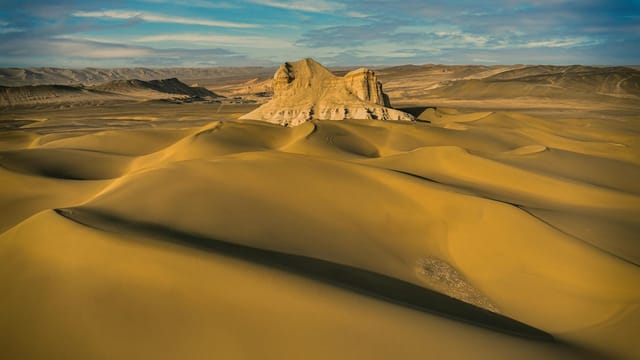 Explore the vast golden dunes and rock formations of Kumtag Desert under a brilliant blue sky.