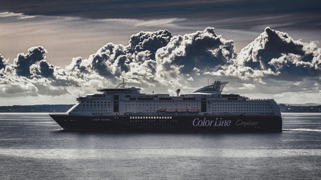 A stunning cruise ship navigates the calm ocean beneath striking, billowing clouds.