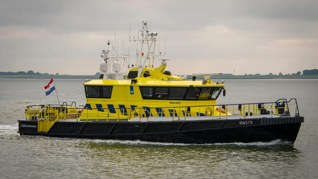 Yellow Dutch coastguard vessel sailing in calm waters near Terneuzen, Netherlands.