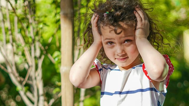 Curly-haired girl in playful mood outdoors with sunlight filtering through trees, capturing innocence and joy.