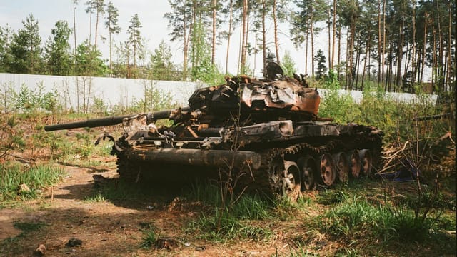A destroyed military tank lies abandoned in a forest near Bucha, Ukraine amidst war-torn surroundings.