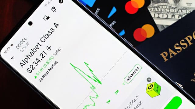 Smartphone displaying stock market app next to U.S. dollar and passport, representing global finance.