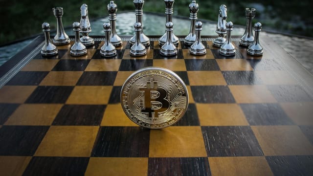 Bitcoin coin standing on a chessboard with silver and brass chess pieces. Concept of strategic digital currency investment.