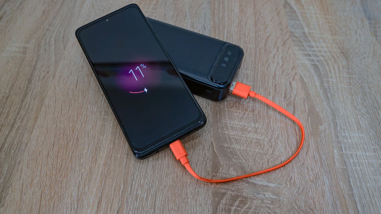 Illustrative image: A smartphone charging from a power bank with an orange cable on a wooden table.